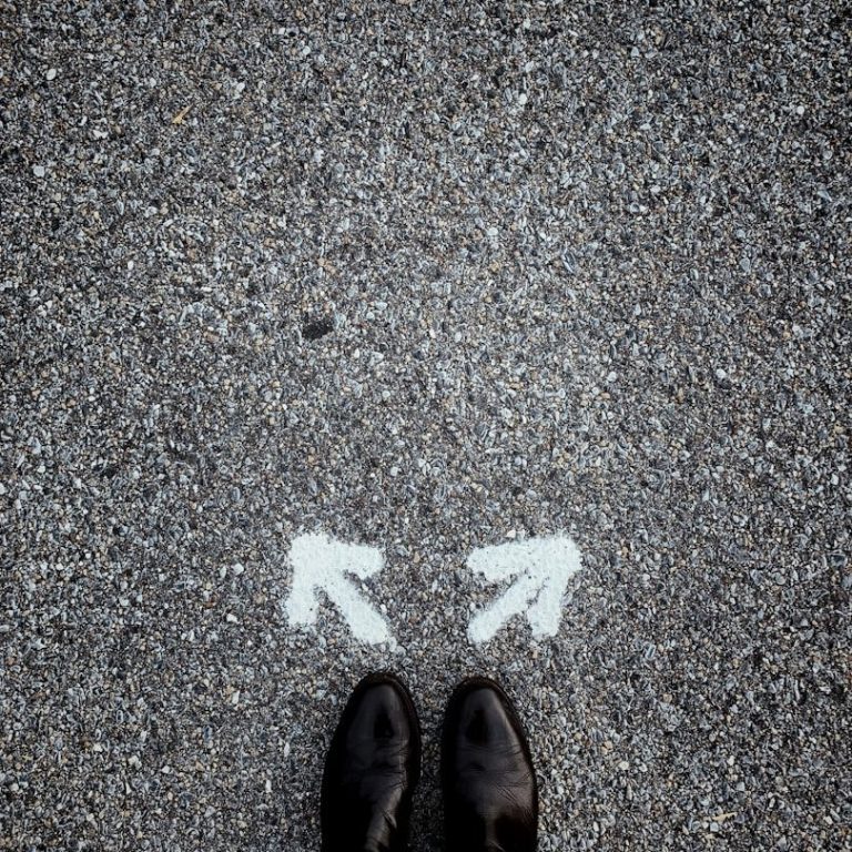 Schwarze Schuhe stehen auf einem Gehweg mit zwei weißen Pfeilen nach links und rechts.