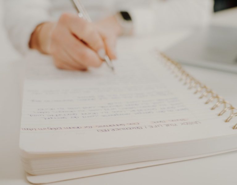 Notizbuch Eine Hand schreibt in ein Notizbuch mit Spiralbindung.