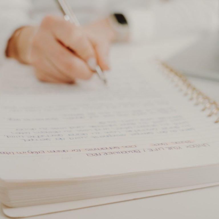 Eine Hand schreibt Notizen in ein offenes Notizbuch.