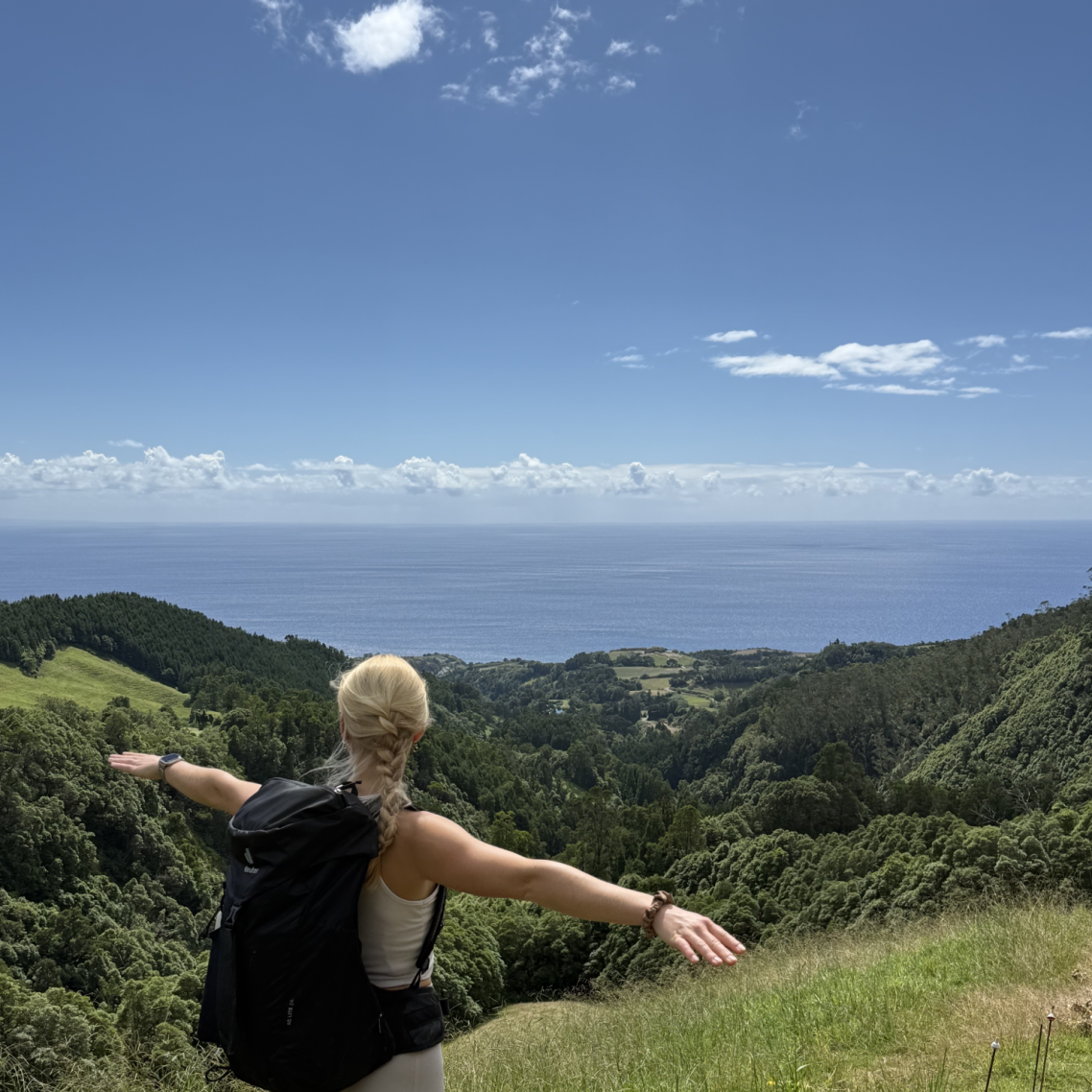 Titelbild Fitness & Ernährung Person mit offenen Armen vor einer Küstenlandschaft und blauem Himmel.