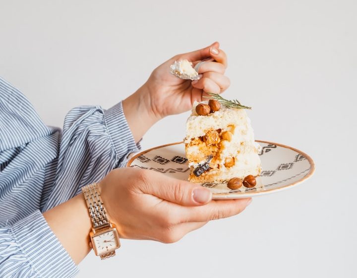 Hand mit Gabel hält ein Stück Torte auf einem dekorativen Teller.
