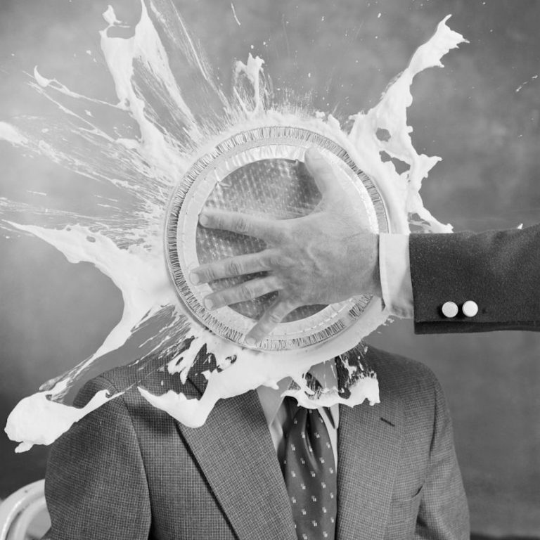 Ein Mann in Anzug wird mit einer Tortenschnitte im Gesicht getroffen.